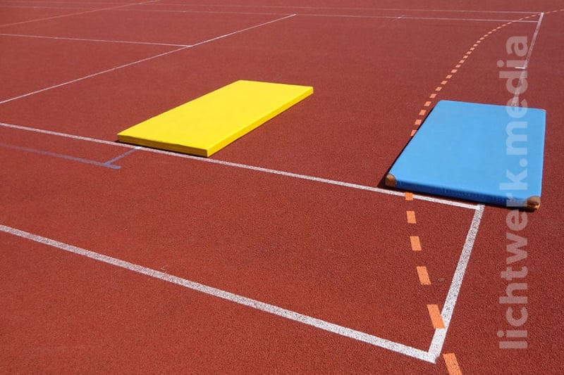 turnmatten unterschiedlicher farbe liegen geometrisch an markierungen ausgerichtet auf sportplatz