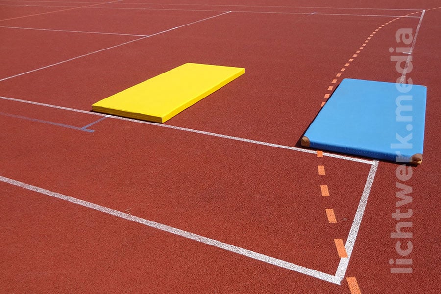 turnmatten unterschiedlicher farbe liegen geometrisch an markierungen ausgerichtet auf sportplatz