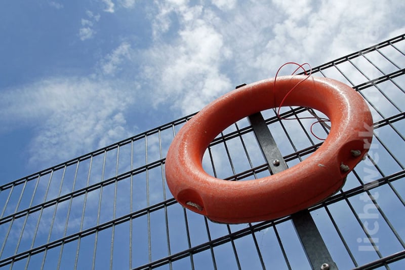 an einem zaun hängender rettungsring, von schräg unten gegen den himmel fotografiert