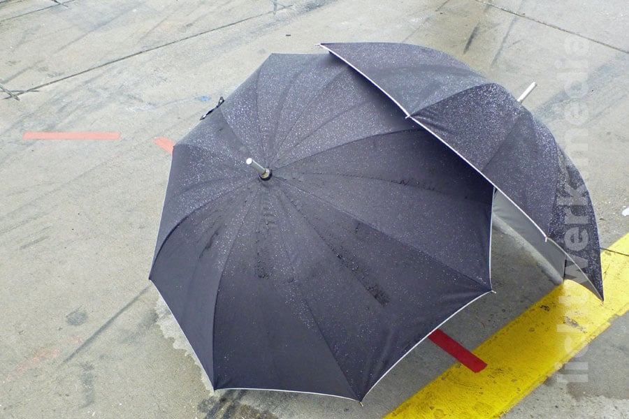 zwei ineinandergestellte regenschirme im regen auf nasser rennbahn